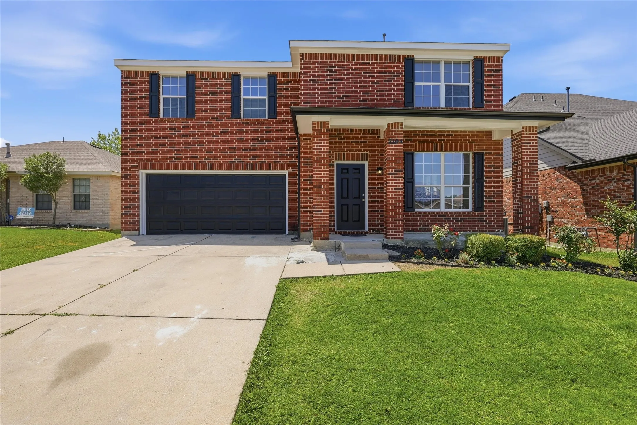Brick facade with a covered entry, black paneled garage door, and a concrete driveway