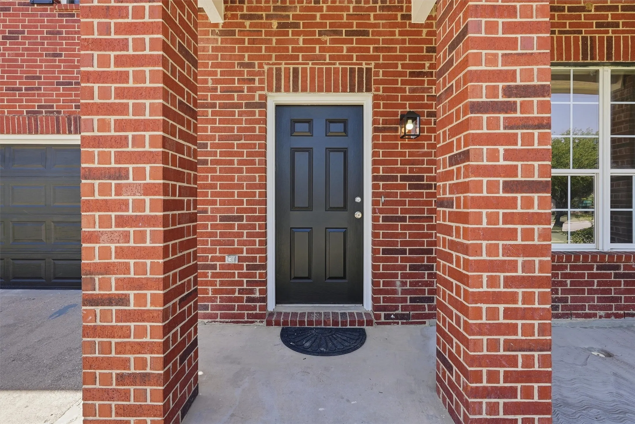 Brick exterior with a dark panel door, covered entry, and exterior lighting fixture