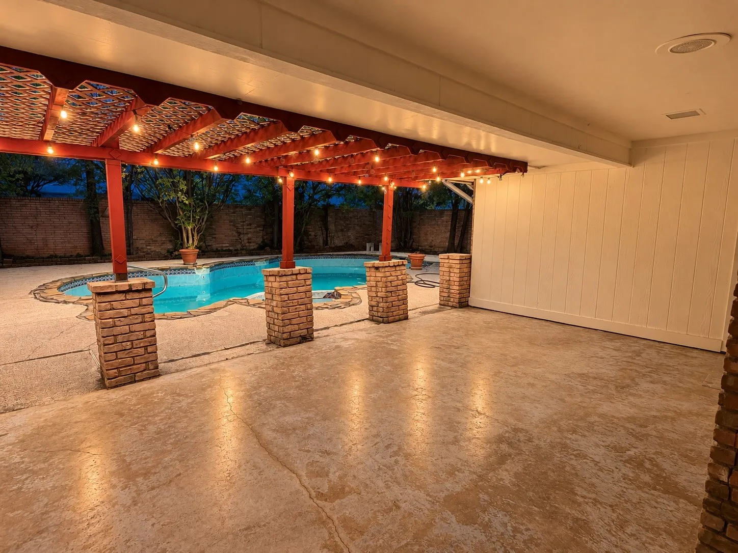 Patio with a large swimming pool, brick-clad support columns, and an expansive covered area featuring a red wood-finish pergola
