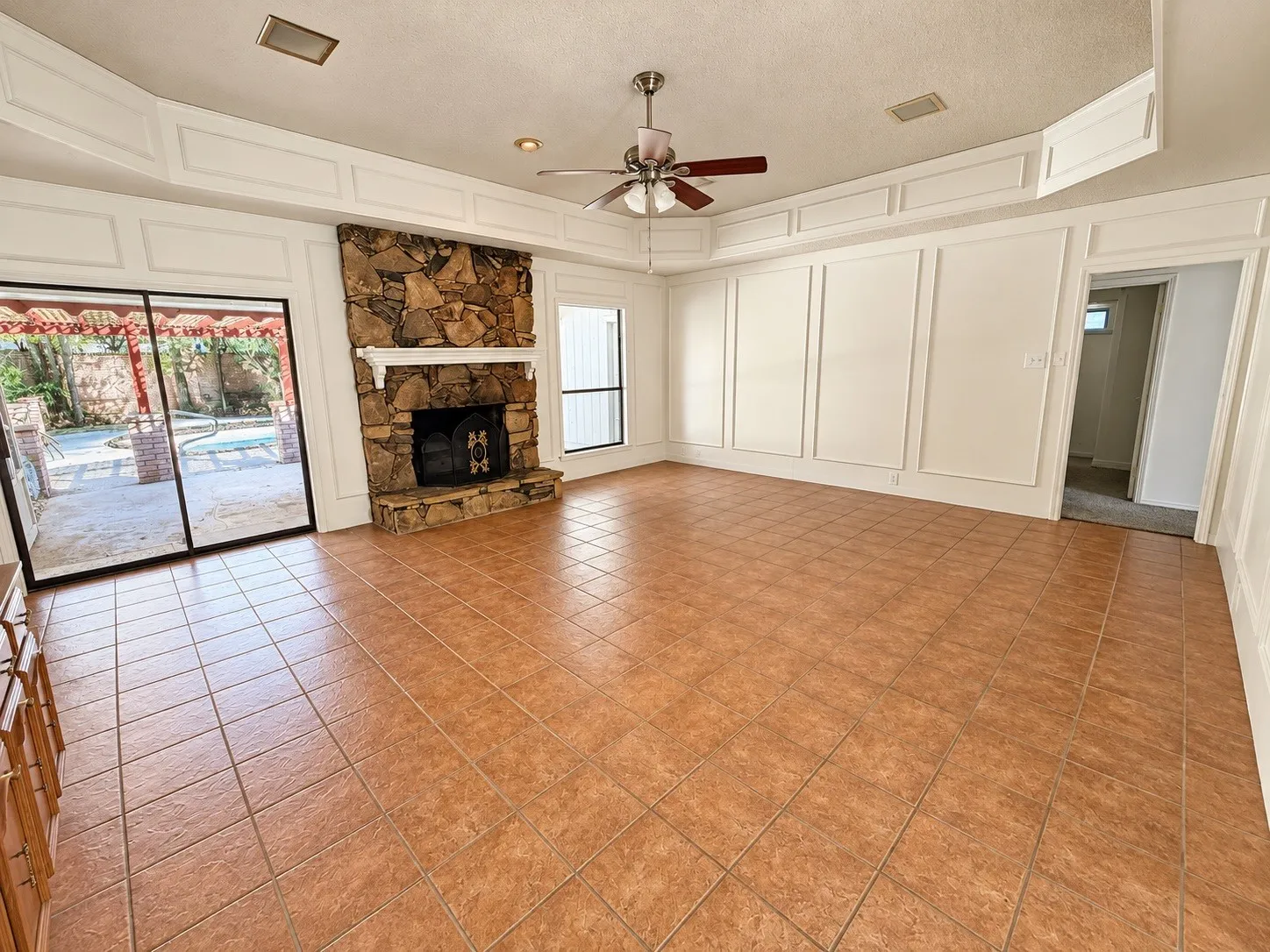 Stone fireplace, tile flooring, decorative wall molding, ceiling fan, and sliding glass doors to the exterior