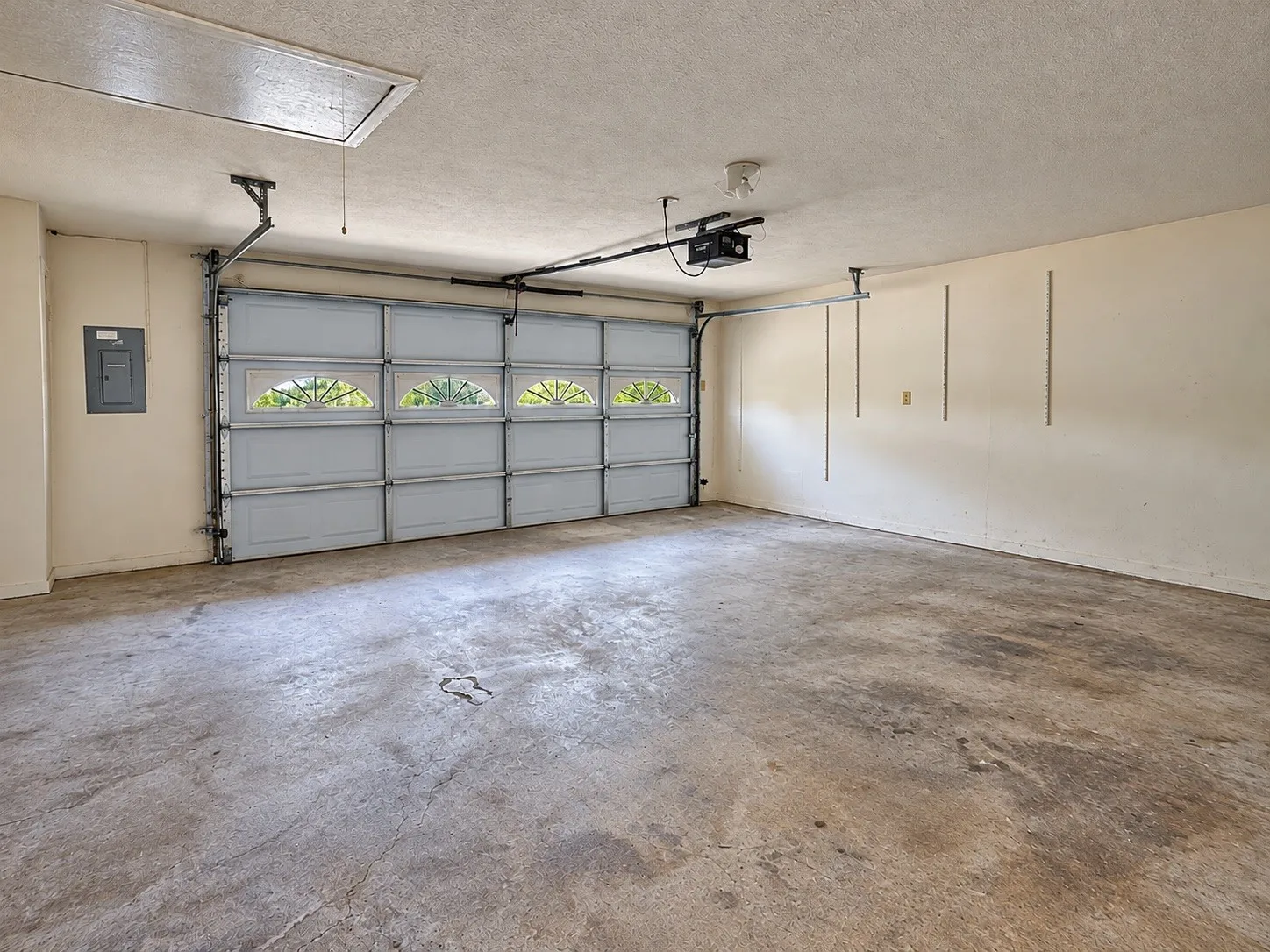 Attached garage featuring a sectional door with frosted arched window inserts, concrete flooring, and an overhead access panel