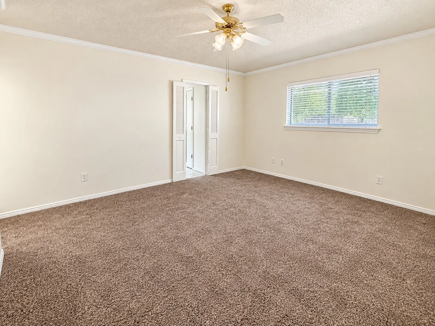 Neutral-toned carpet flooring, a ceiling fan with integrated lighting, and crown molding