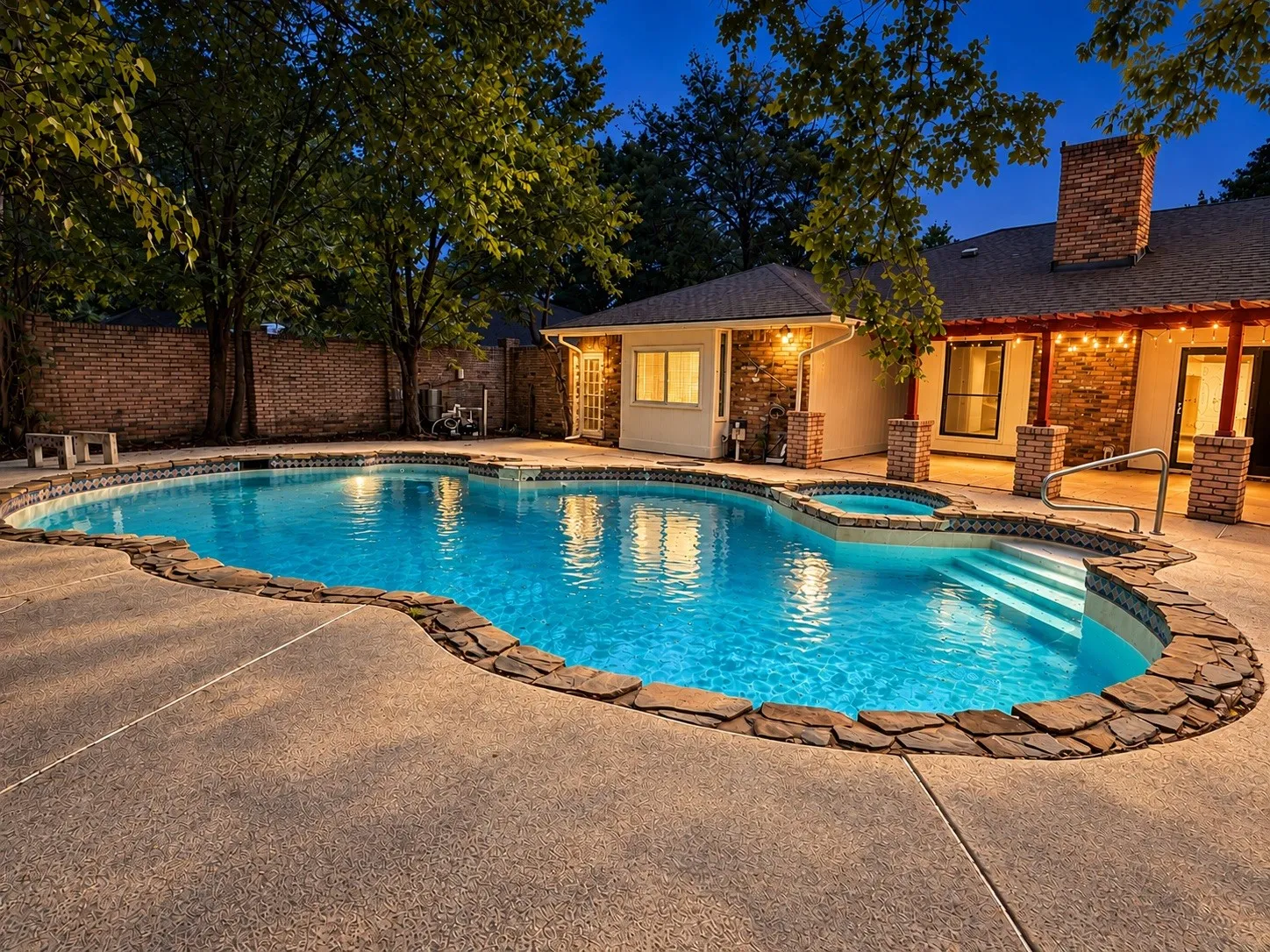 Kidney-shaped swimming pool with an integrated spa, stone coping, and concrete decking