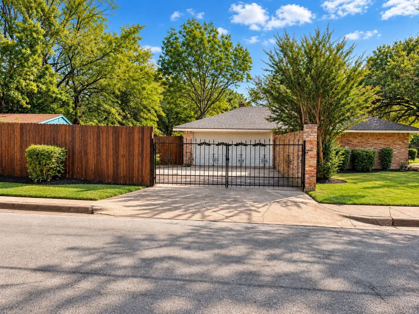Wrought iron gate with brick pillars, leading to an attached garage with a decorative door