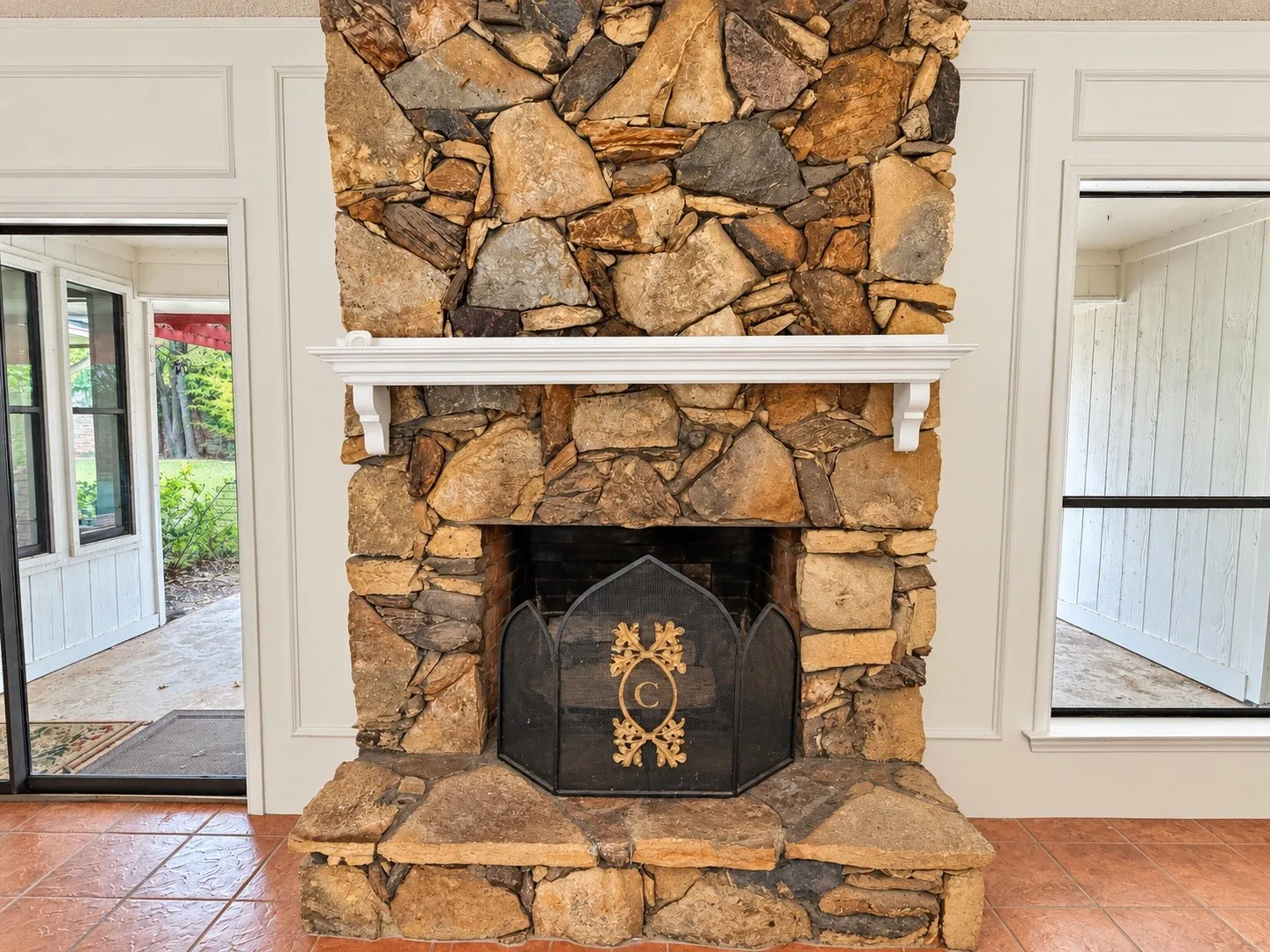 Natural stone fireplace with a white mantel, terracotta floor tiles, and panel molding trim