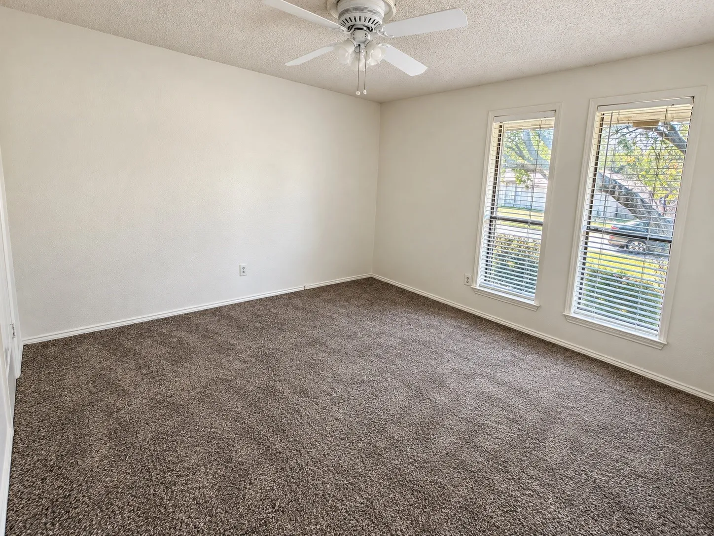 Neutral wall finishes, textured ceiling, ceiling fan, carpeted flooring, and two windows with blinds