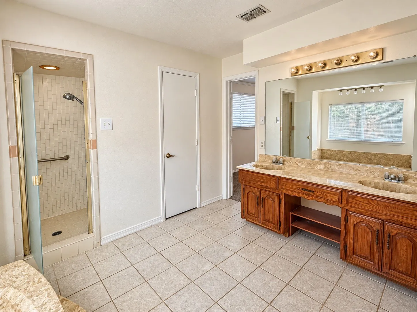 Dual vanity with integrated sinks and a stone countertop, individual mirrors, a shower enclosure with a glass door, and tiled flooring