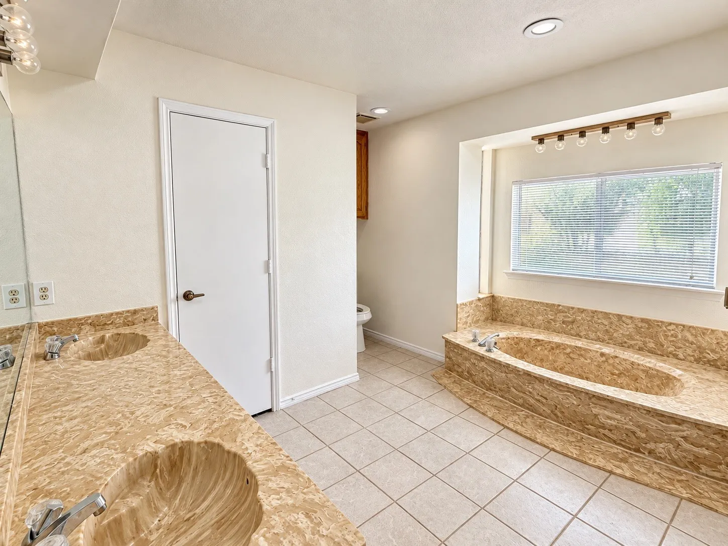 Dual vanity with integrated shell-shaped sinks, tiled flooring, and a built-in soaking tub with a window