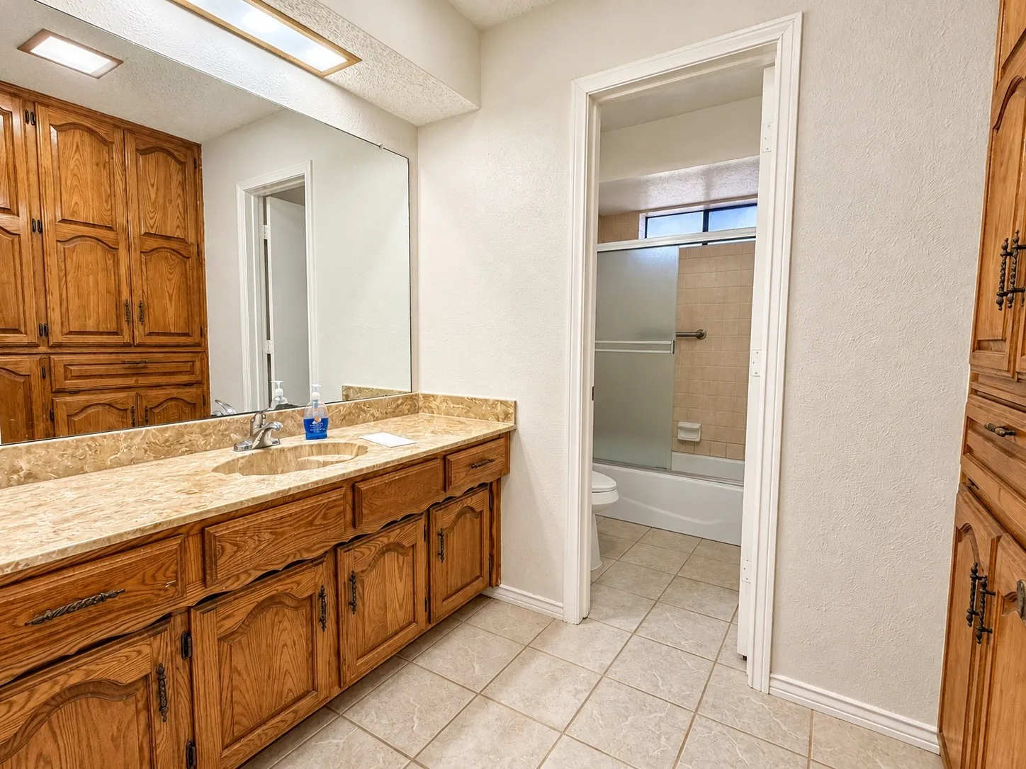 Extended vanity featuring an integrated sink with a polished chrome faucet, substantial mirror, and wood-finish cabinetry