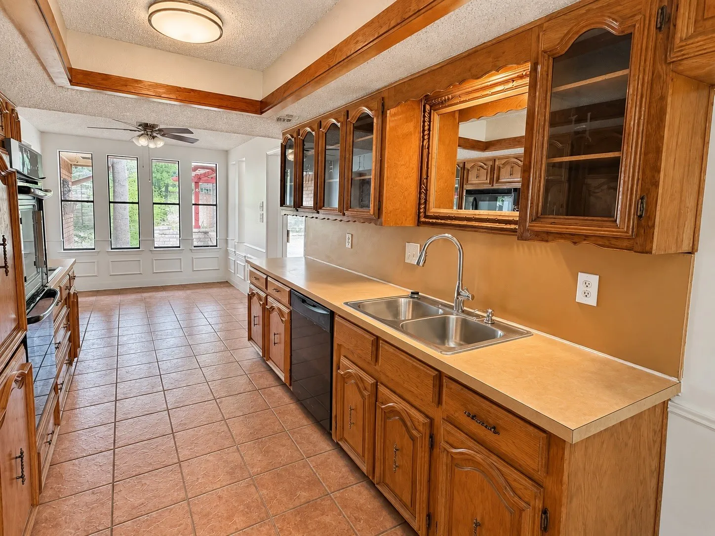 Kitchen featuring wood cabinetry, a double basin stainless steel sink with a gooseneck faucet, light-toned countertops, and tile flooring