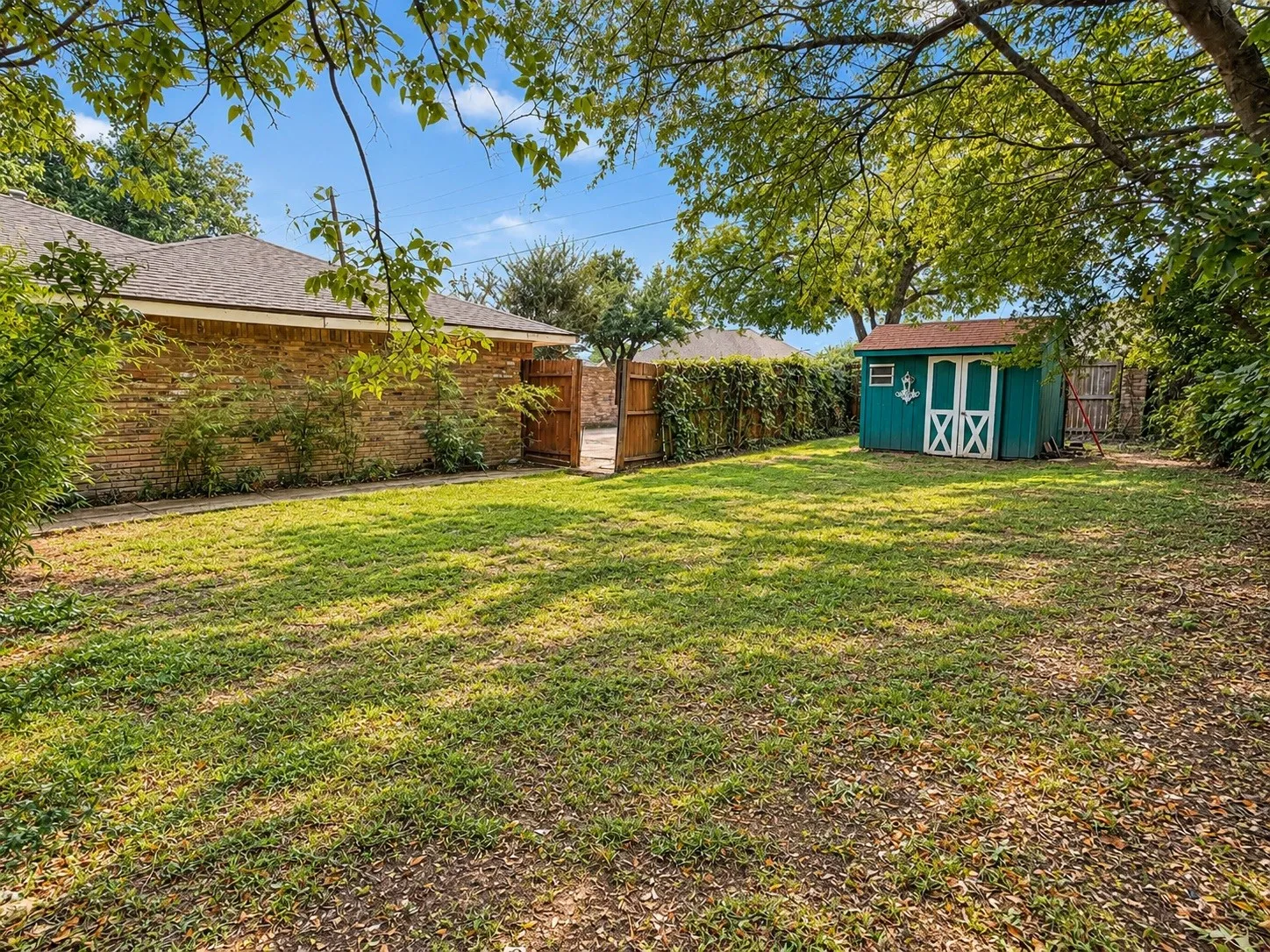 Expansive grassy yard with mature trees, a detached storage shed, and a brick exterior wall