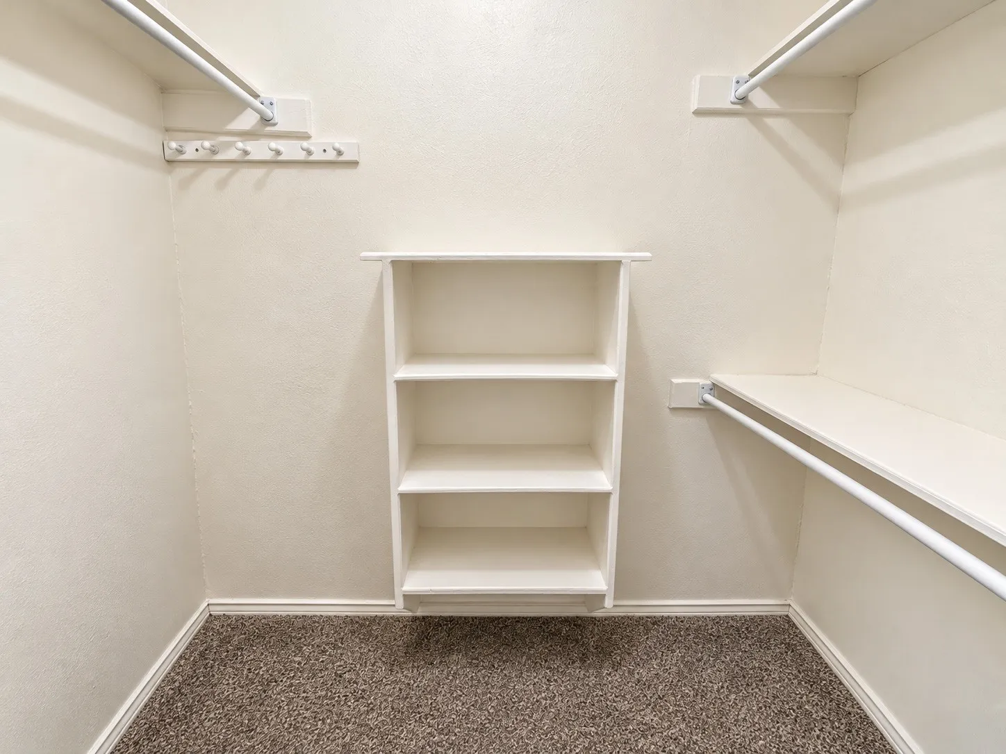 Built-in shelving, integrated hanging rods, wall-mounted hooks, and carpeted flooring