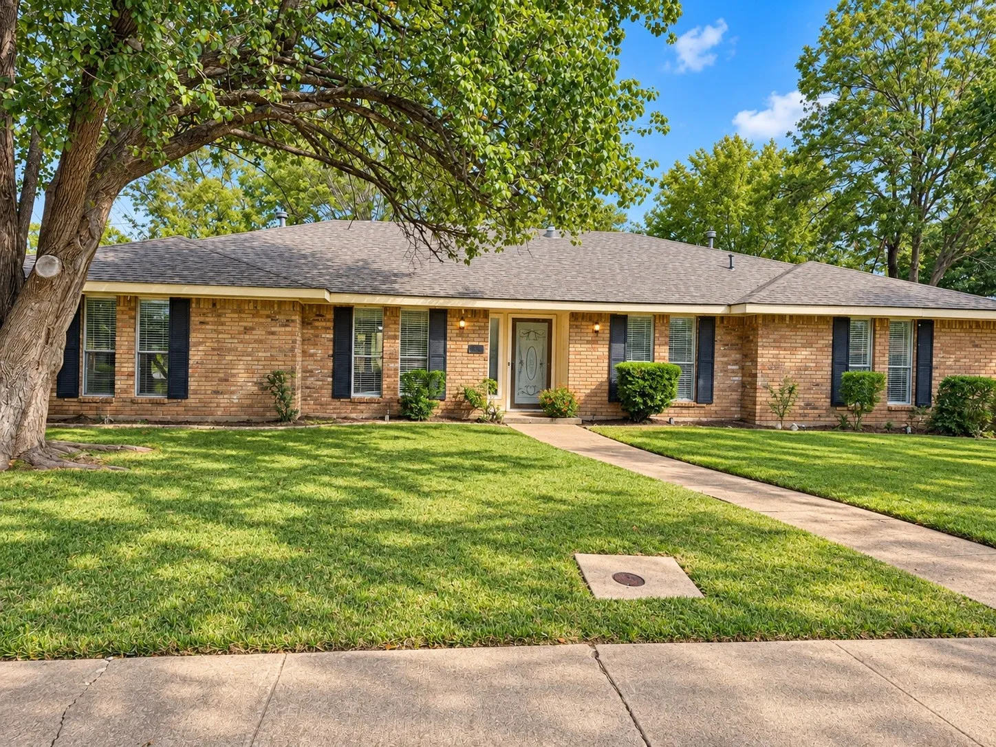 Brick exterior with dark shutters, a front walkway, and a dark shingle roof