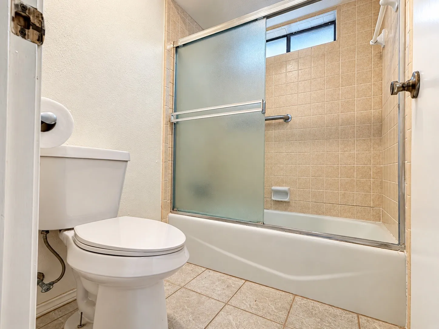 Bathroom featuring a white toilet, tiled flooring, tiled shower surround, and a glass-paneled tub enclosure