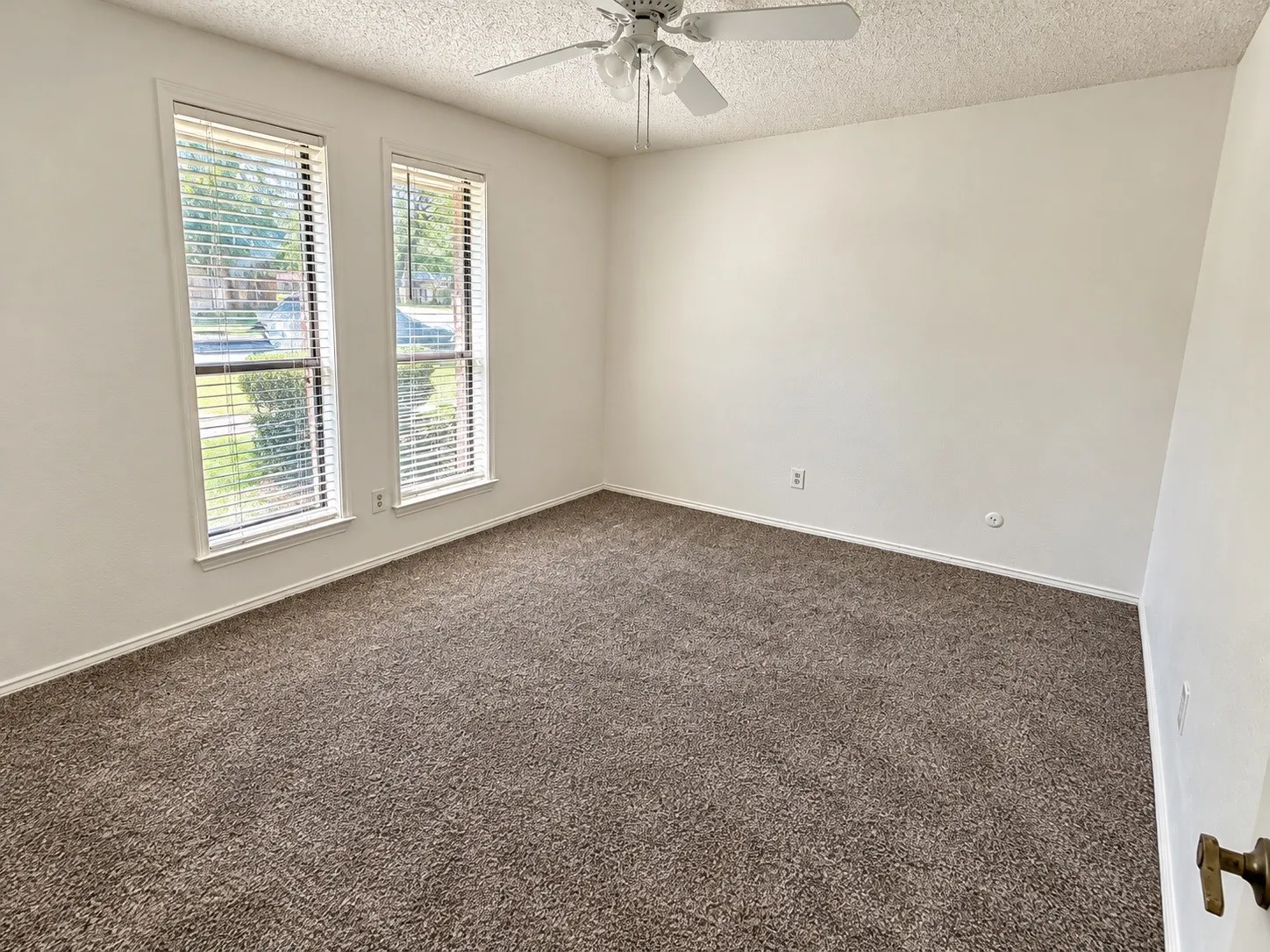 Neutral-toned walls, brown carpeting, and a ceiling fan