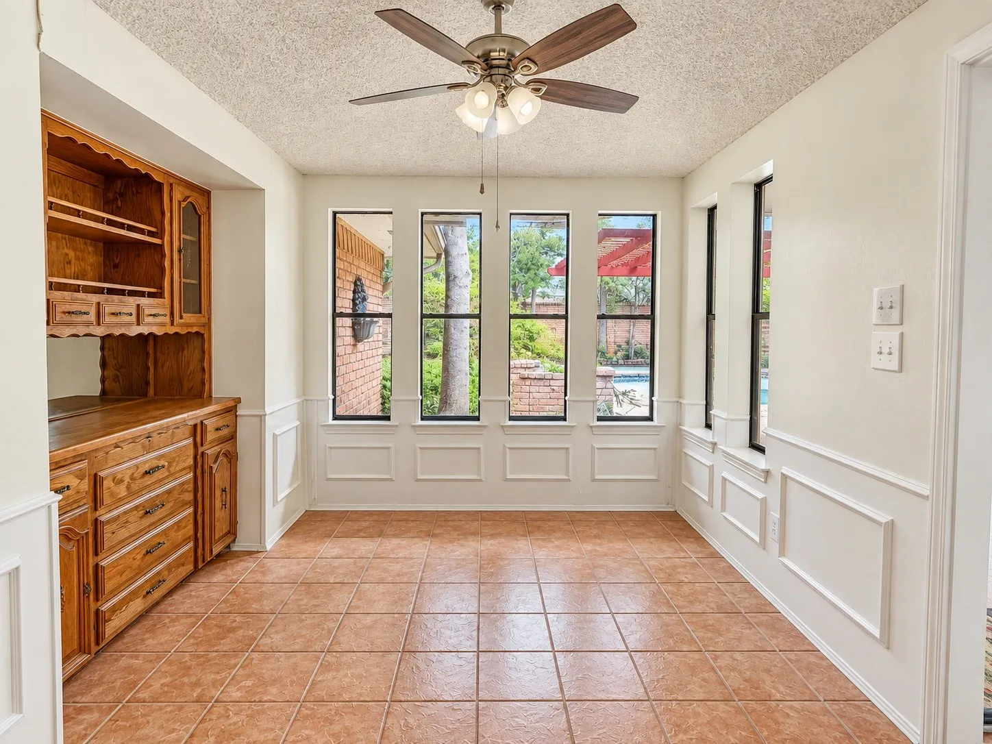 Built-in wood cabinetry with glass-front display, tile flooring, and multiple windows with white trim