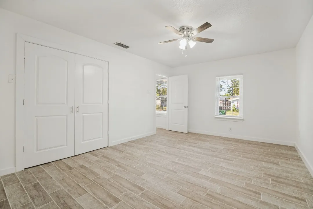 Wood-finish flooring, white walls, double-door closet, ceiling fan with light, and multiple windows