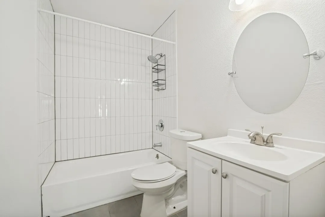 Bathroom featuring a white vanity with integrated sink, brushed nickel faucet, oval mirror, and a white bathtub with subway tile surround