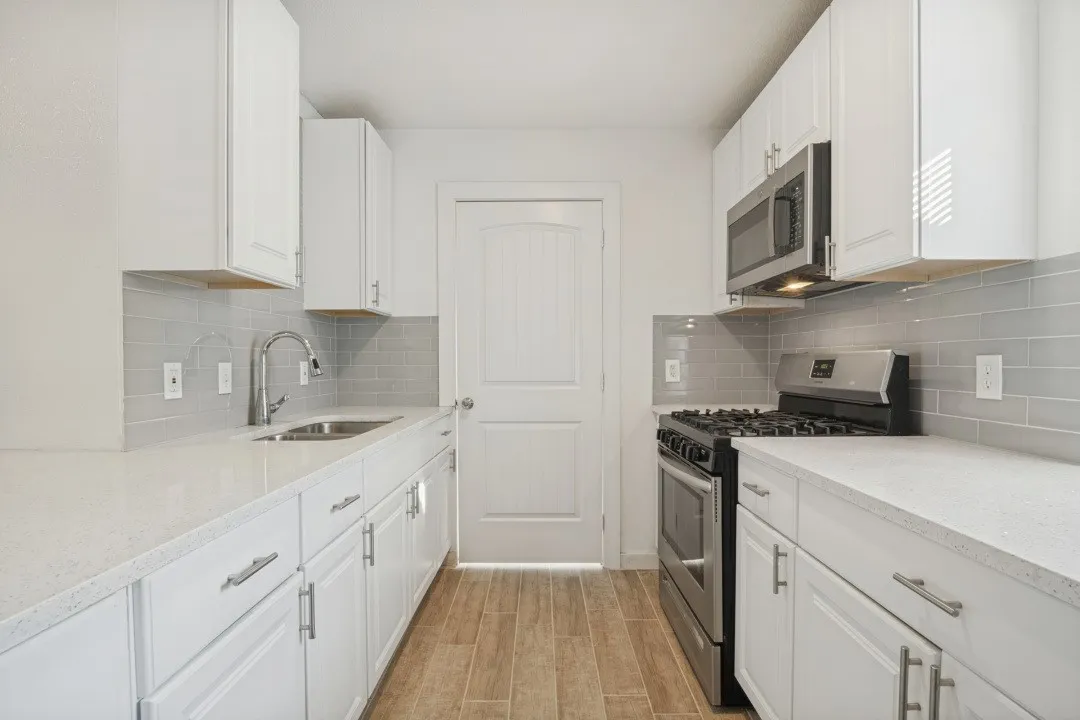 White cabinetry with brushed nickel hardware, stainless steel appliances, stone countertops, gray subway tile backsplash, and wood-finish flooring