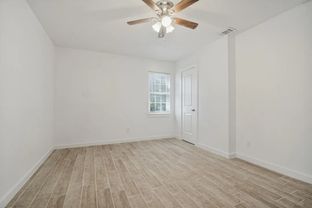 Wood-finish plank flooring, ceiling fan with integrated lighting, white interior door, and window with natural light