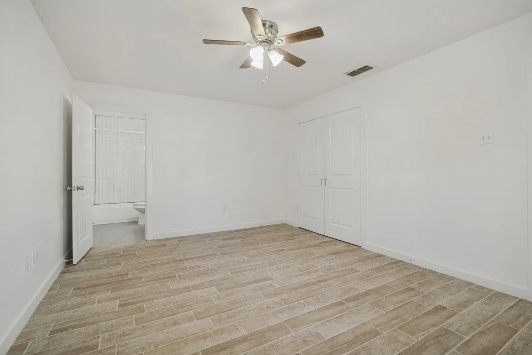 Spacious room featuring wood-finish tile flooring, ceiling fan with integrated lighting, and white bi-fold closet doors