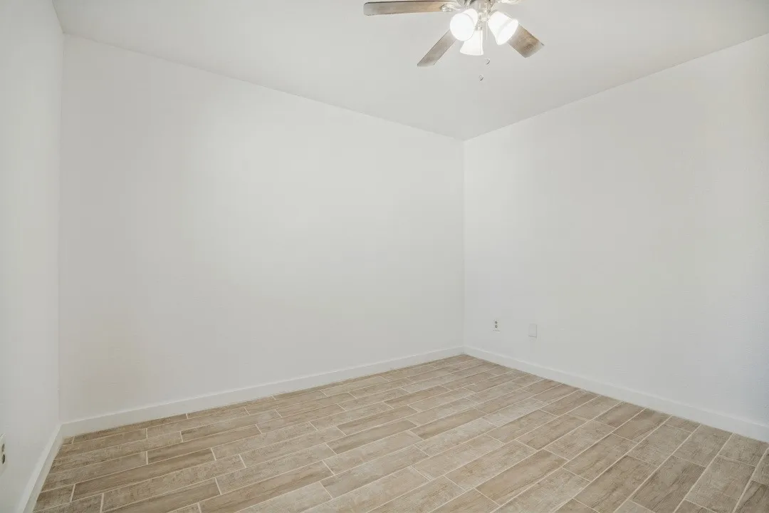 Wood-finish flooring with white baseboards, light neutral wall paint, and a ceiling fan with integrated lighting
