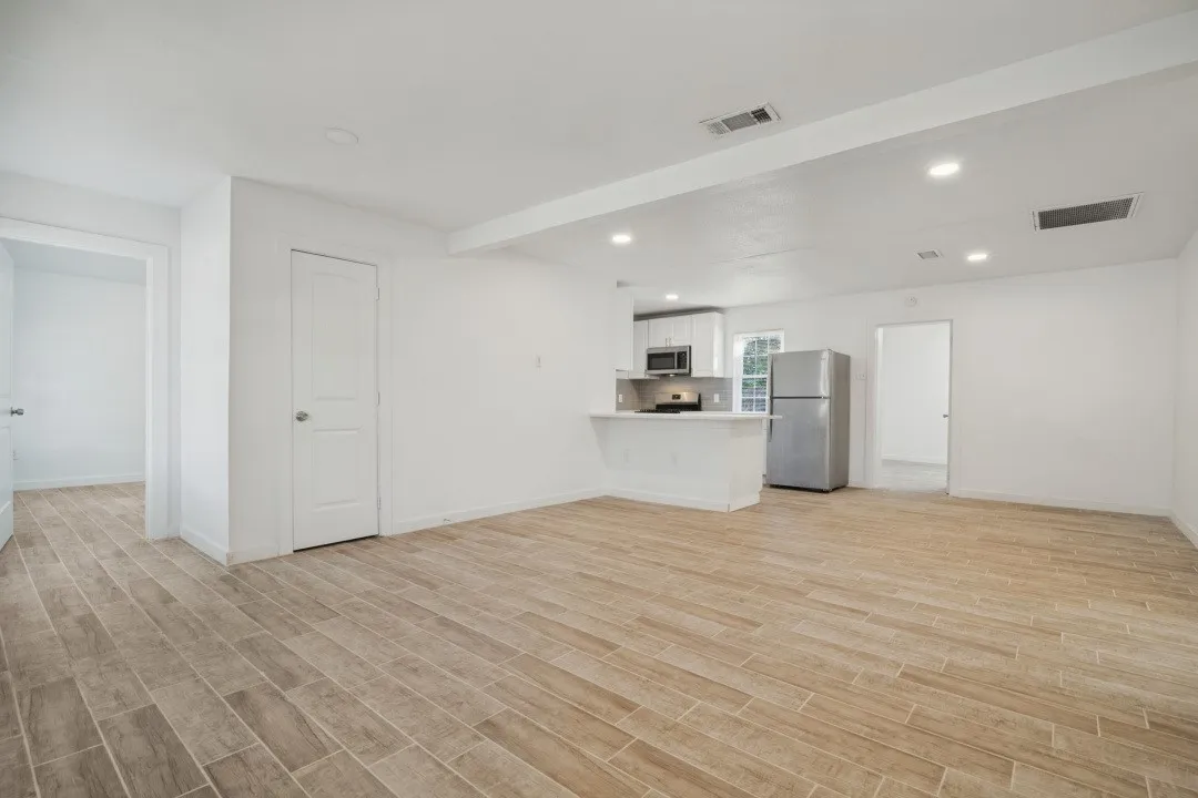 Open-concept living area with wood-finish flooring, recessed lighting, and a kitchen featuring stainless steel appliances and white cabinetry