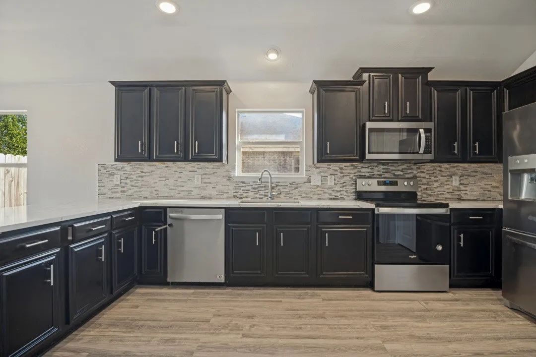 Kitchen featuring dark wood cabinetry, light countertops, wood-finish flooring, a mosaic tile backsplash, and stainless steel appliances