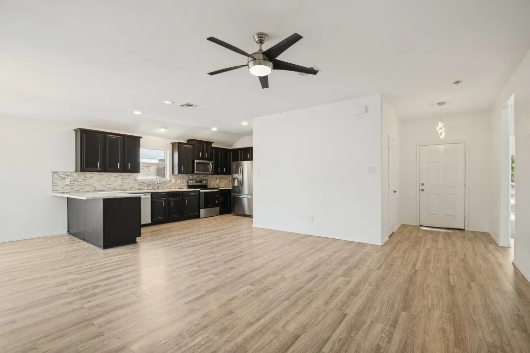Open-concept common area featuring wood-finish flooring, dark wood cabinetry, a mosaic tile backsplash, and stainless steel appliances