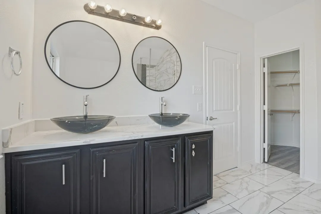 Dual vessel sinks, black cabinetry, white countertop, two circular mirrors, and tile flooring