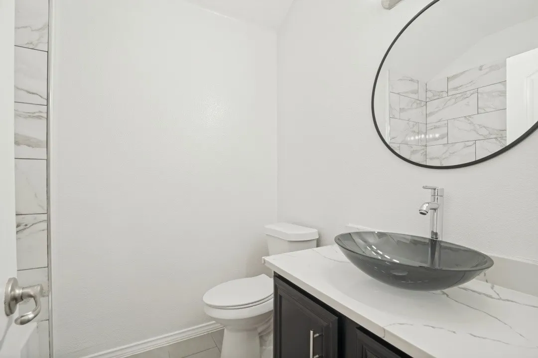 Vanity with a vessel sink, a chrome-finish faucet, and a round mirror