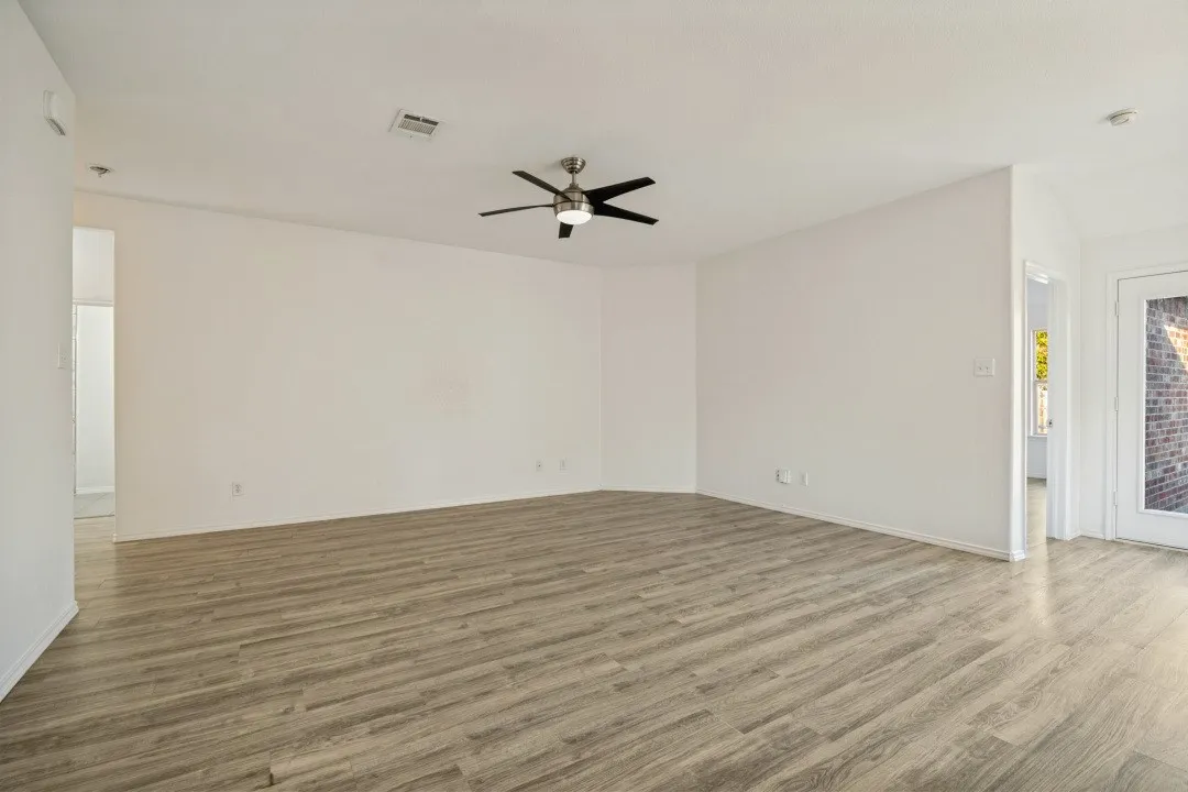 Spacious room featuring wood-finish flooring, a ceiling fan with integrated lighting, and white painted walls