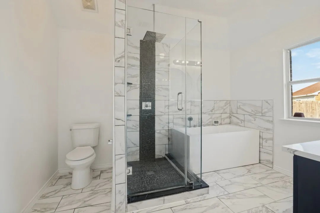 Glass-enclosed shower with black tile surround, white soaking tub, and white tile flooring