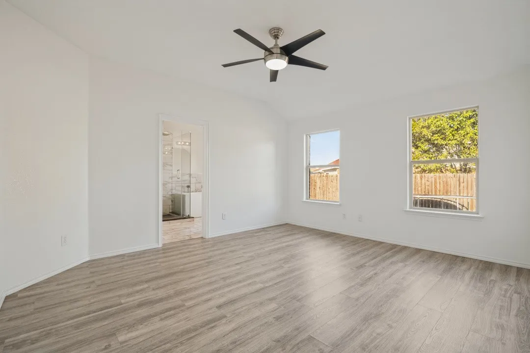Vaulted ceiling with a contemporary ceiling fan, wood-finish flooring, two windows, and an en-suite bathroom featuring a double vanity with ample lighting