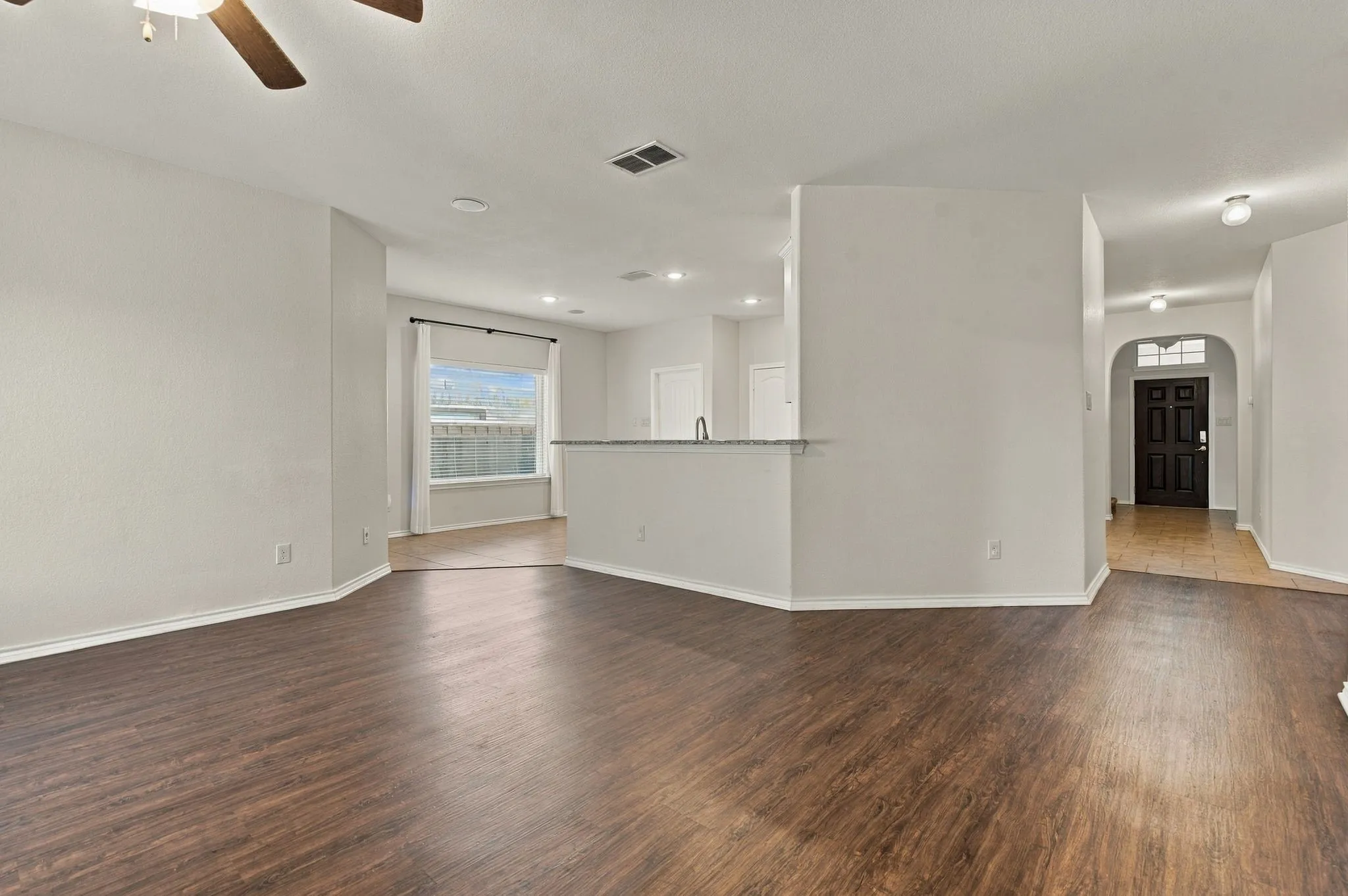 Wood-finish flooring, ceiling fan, recessed lighting, privacy fencing, and an arched entryway