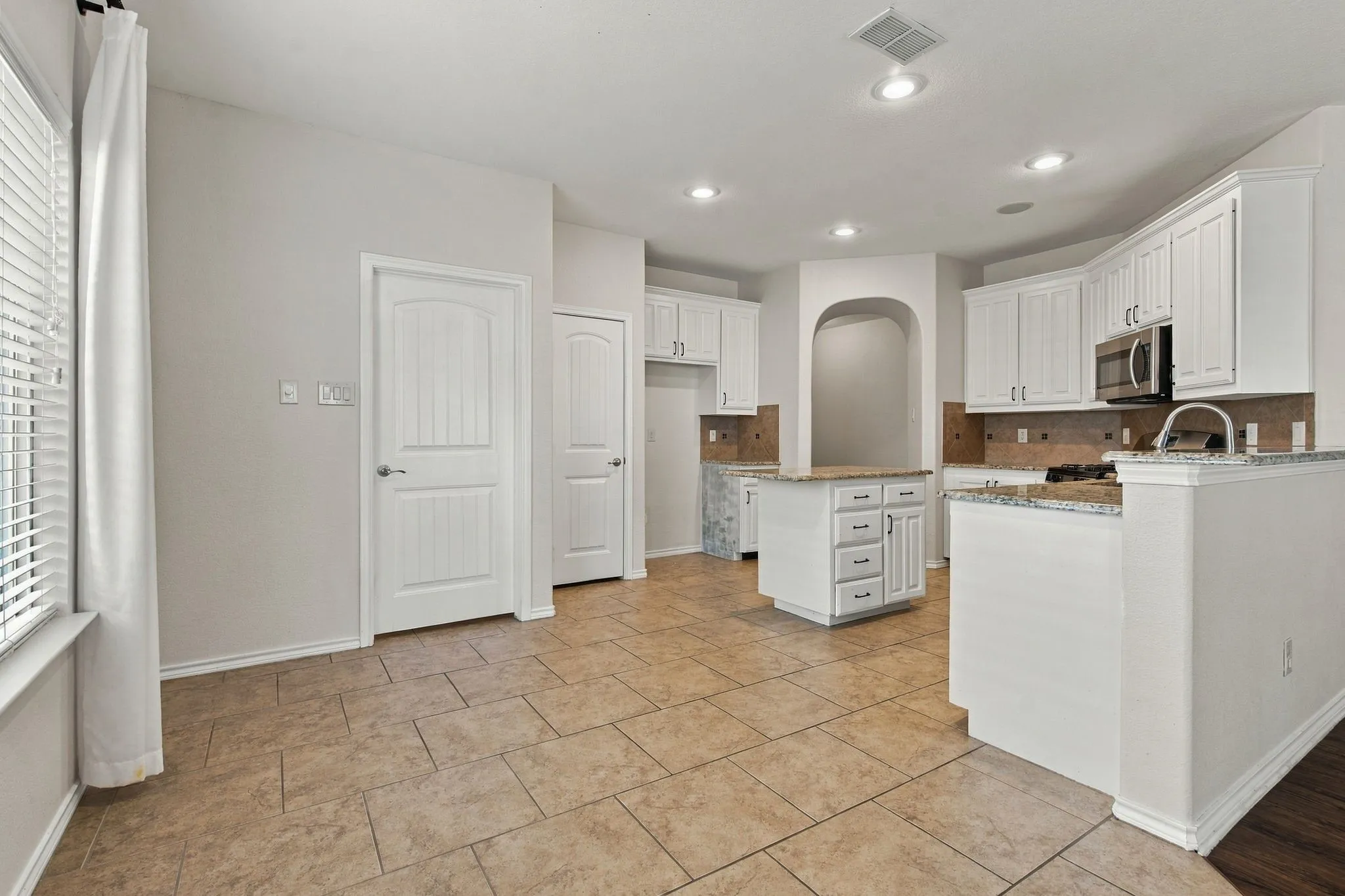 Spacious kitchen featuring white cabinetry, stainless steel appliances, granite countertops, and tile flooring