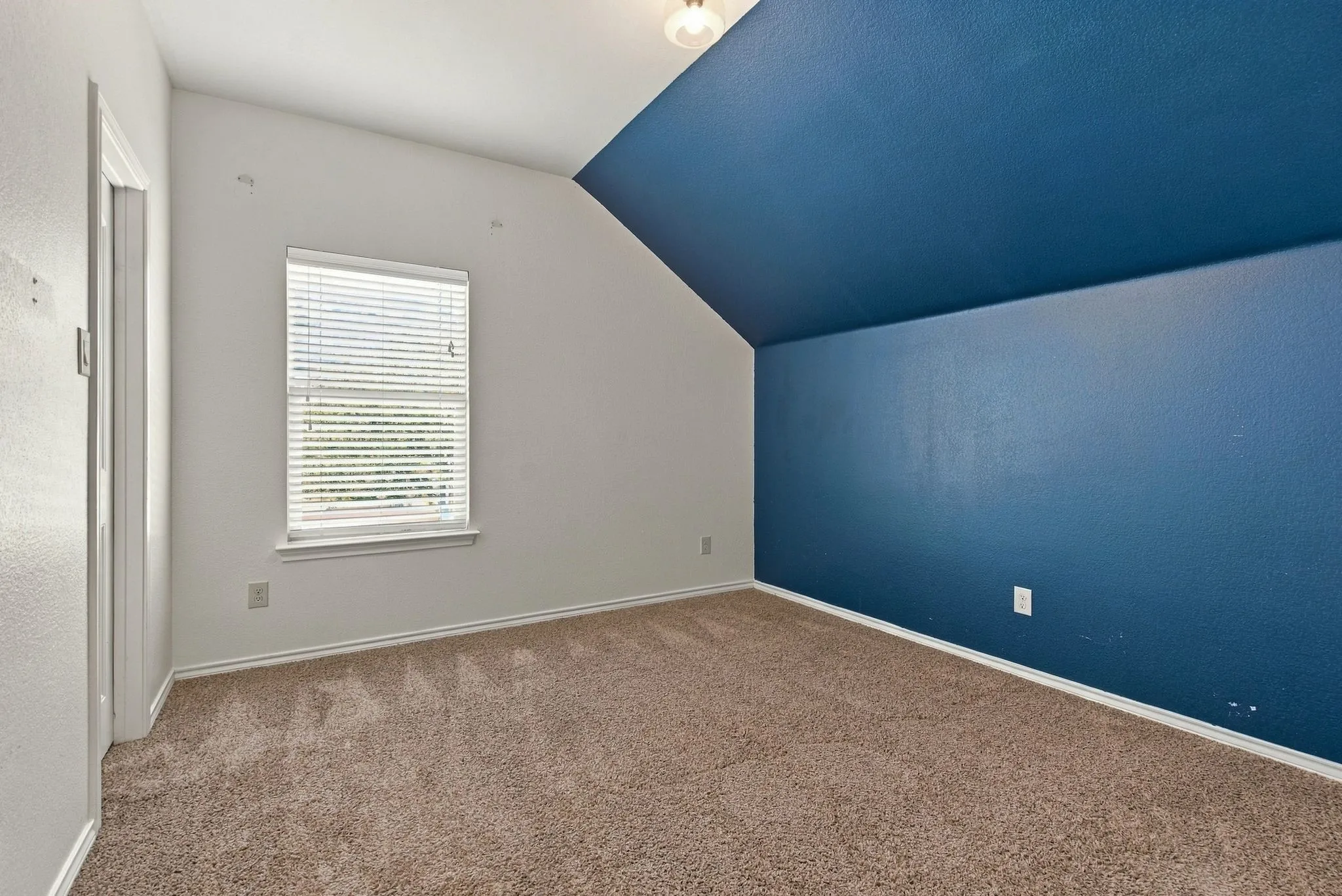 Carpeted flooring, sloped ceiling, window with blinds, overhead lighting fixture, and a painted accent wall