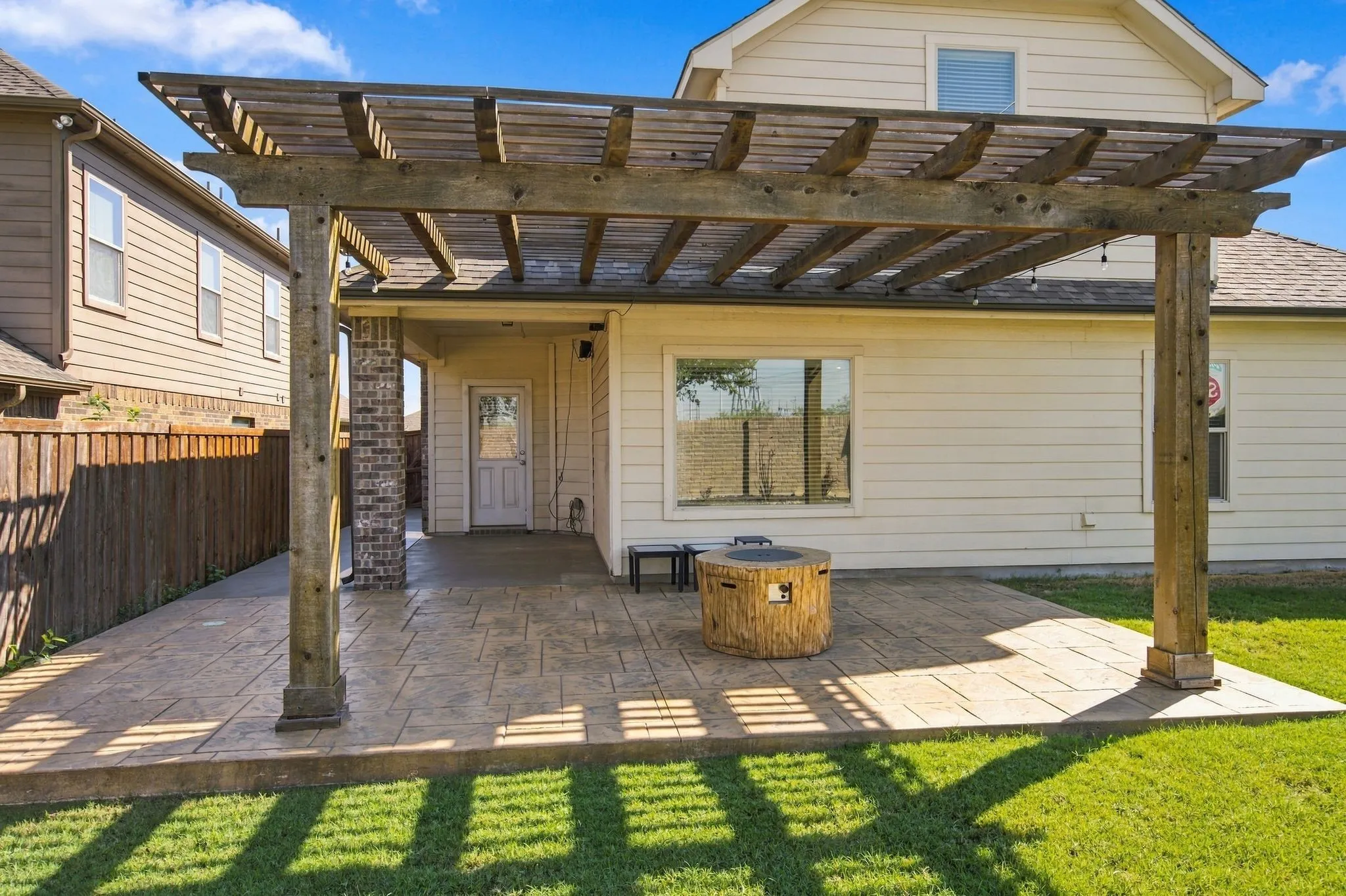 Backyard patio featuring a wooden pergola, stamped concrete, and a covered porch with brick accents