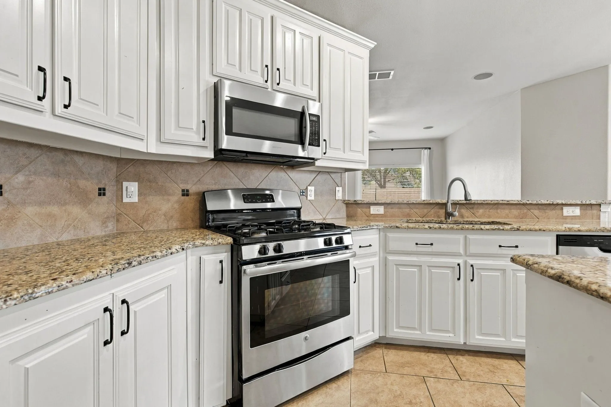 White cabinetry, stainless steel appliances, granite countertops, tile backsplash, and tile flooring