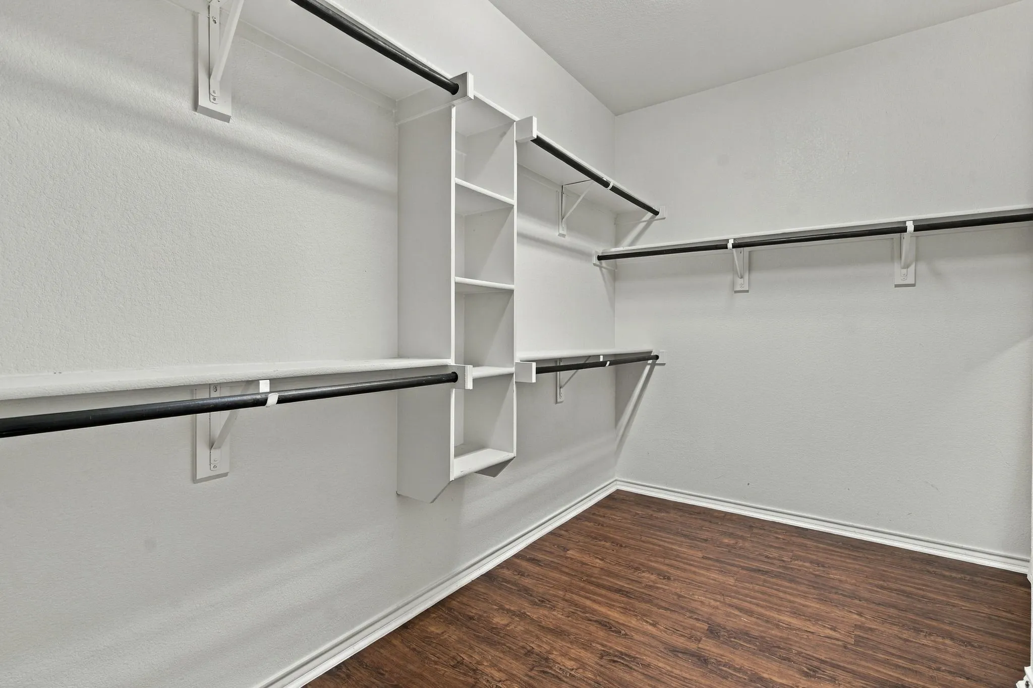 Walk-in closet with multi-level shelving, integrated storage cubbies, multiple hanging rods, and wood-finish flooring