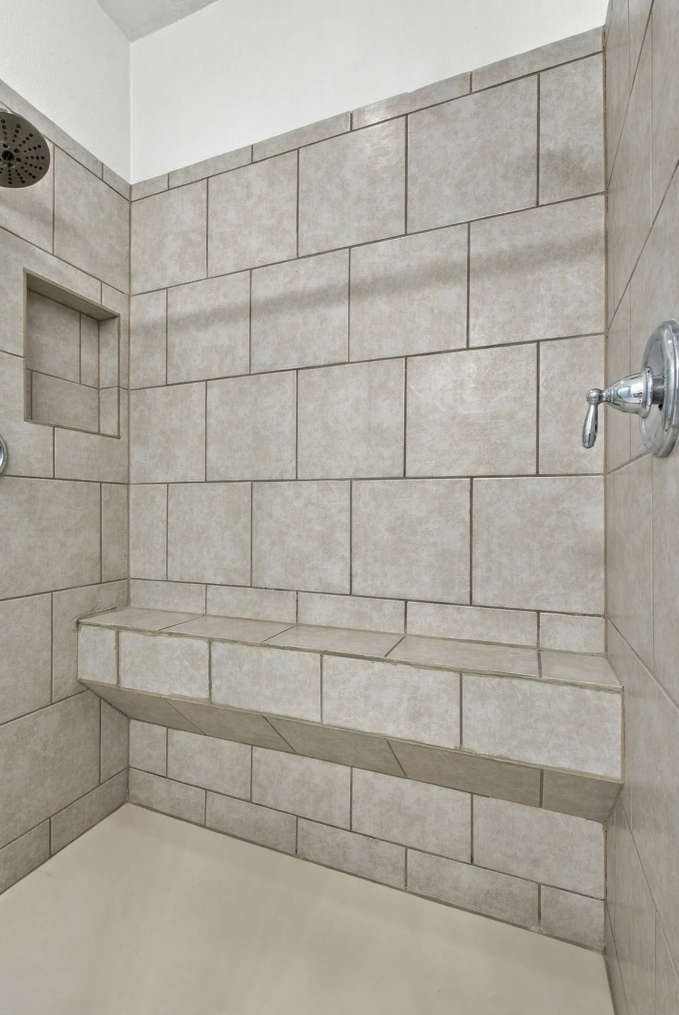 Tiled shower enclosure featuring a built-in bench, recessed niche, and chrome fixtures