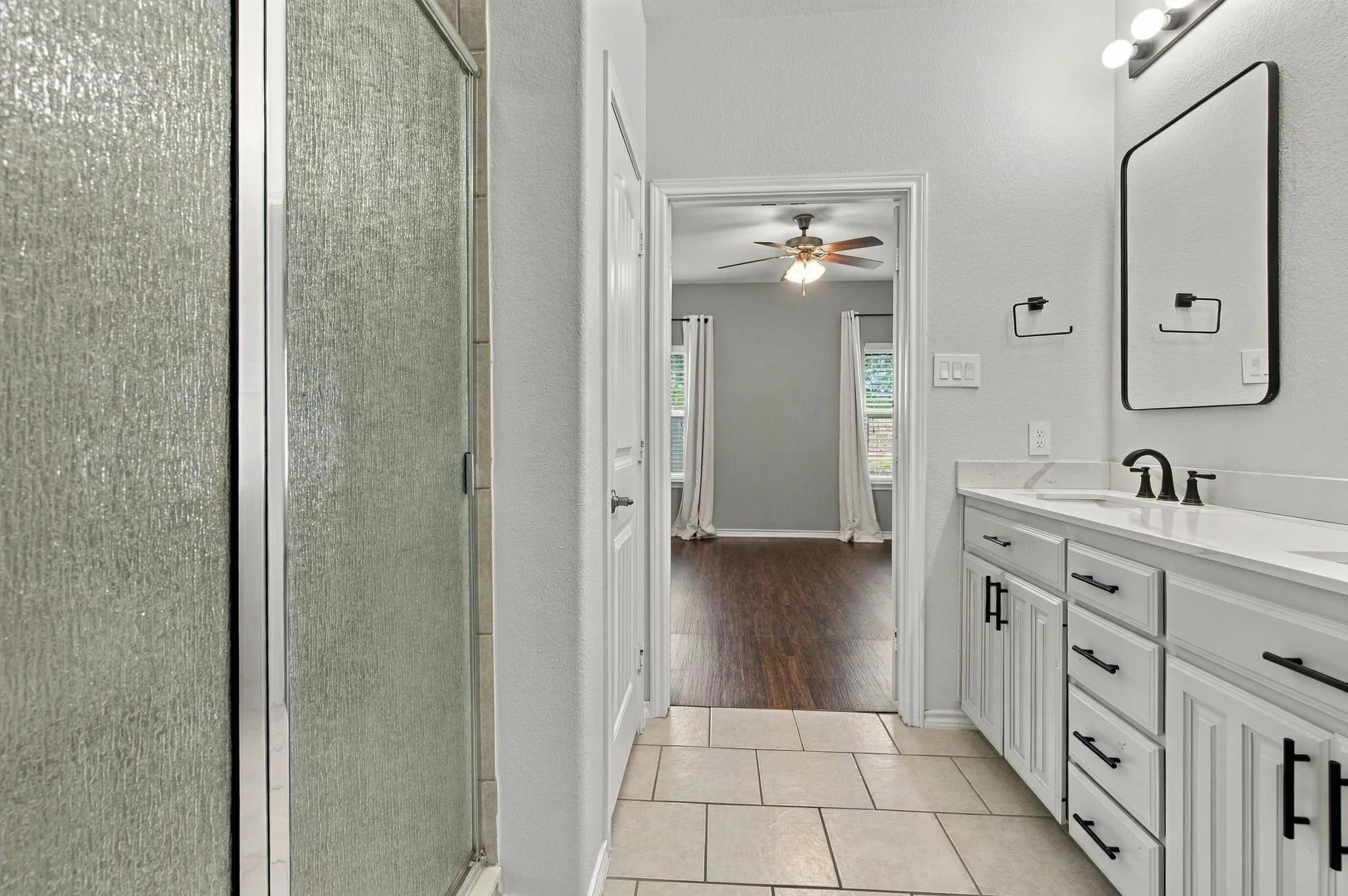 Dual vanity with white cabinetry and black hardware, white countertop, and dark-framed mirror