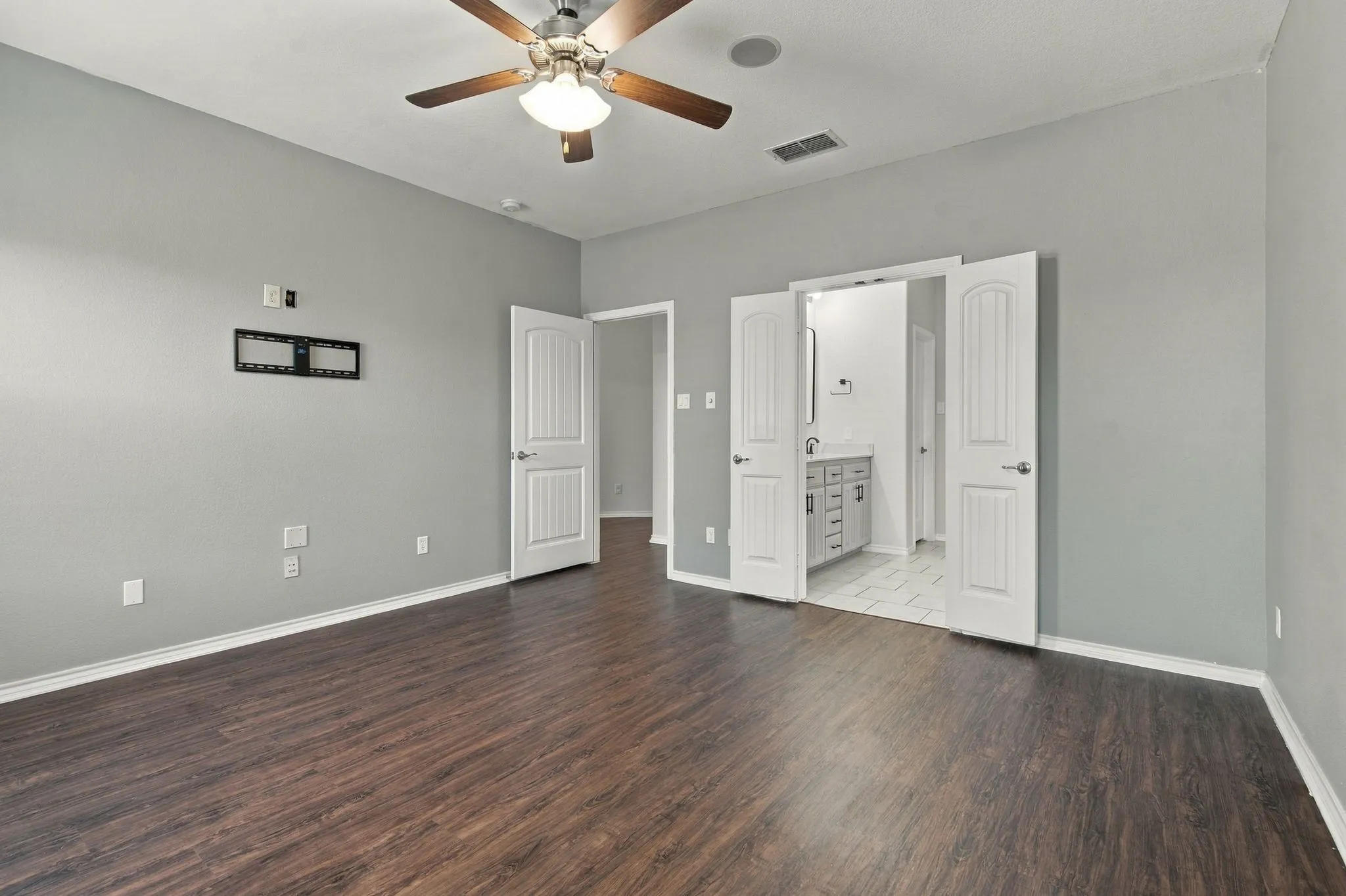 Spacious room featuring wood-finish flooring, light gray walls, and a ceiling fan with integrated lighting