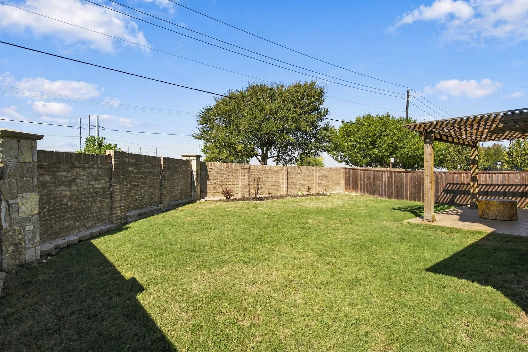 Expansive grassy yard with brick and wood fencing, featuring a stone column and a pergola-covered patio area