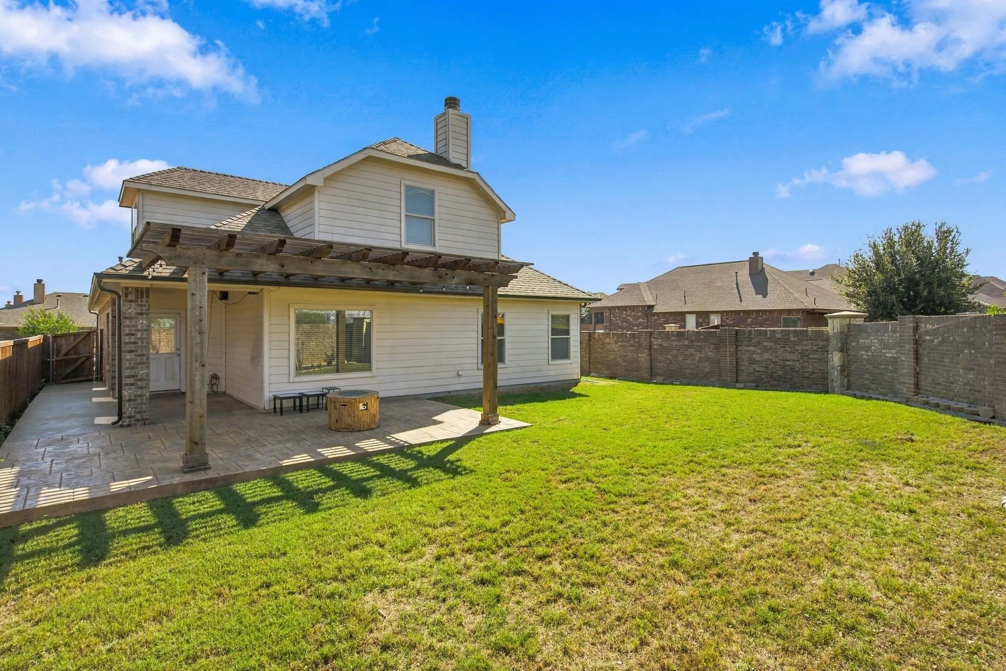 Expansive backyard featuring a pergola-covered stamped concrete patio, stone column accents, and a large grassy area
