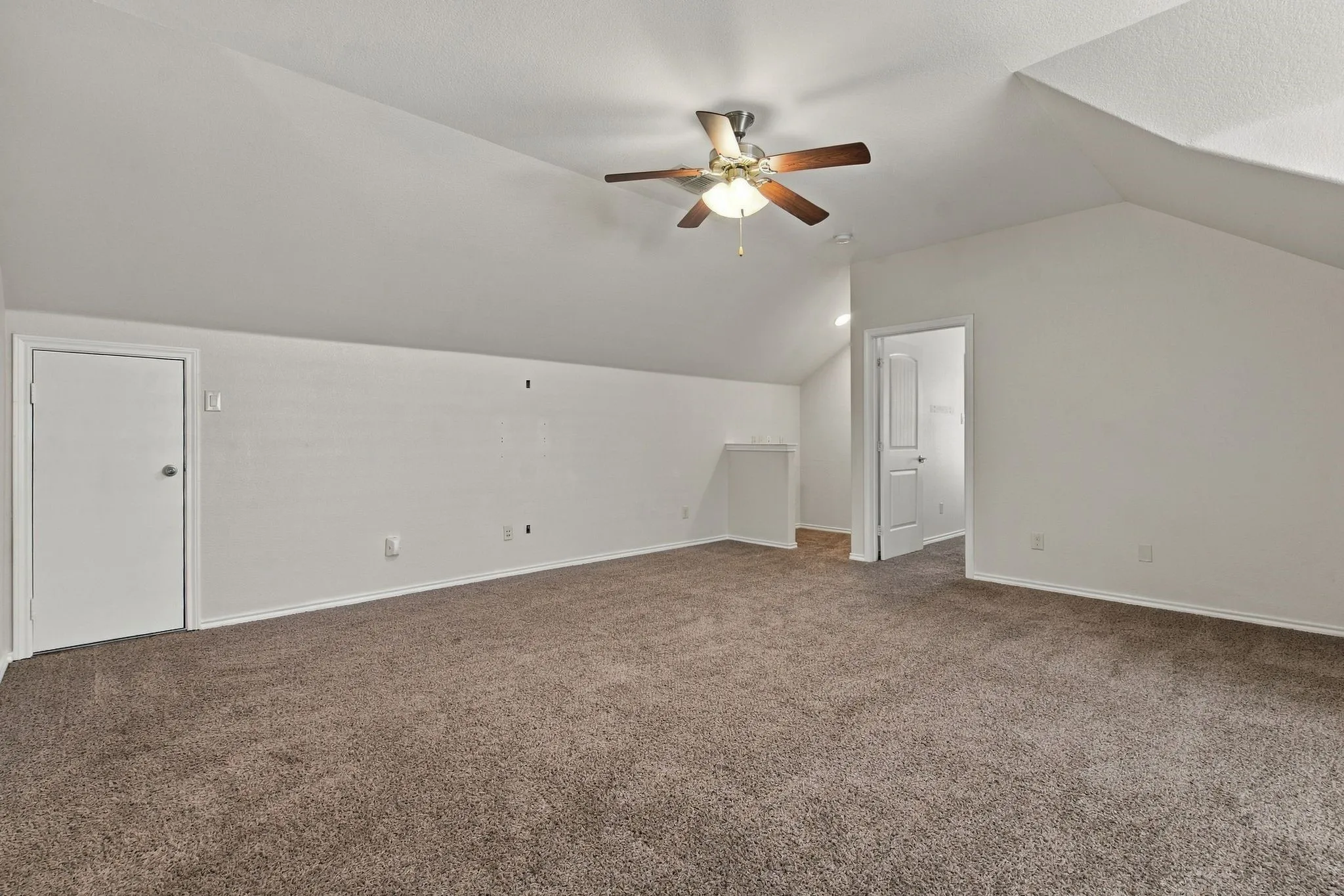 Sloped ceilings with a ceiling fan, plush carpet, and a solid door