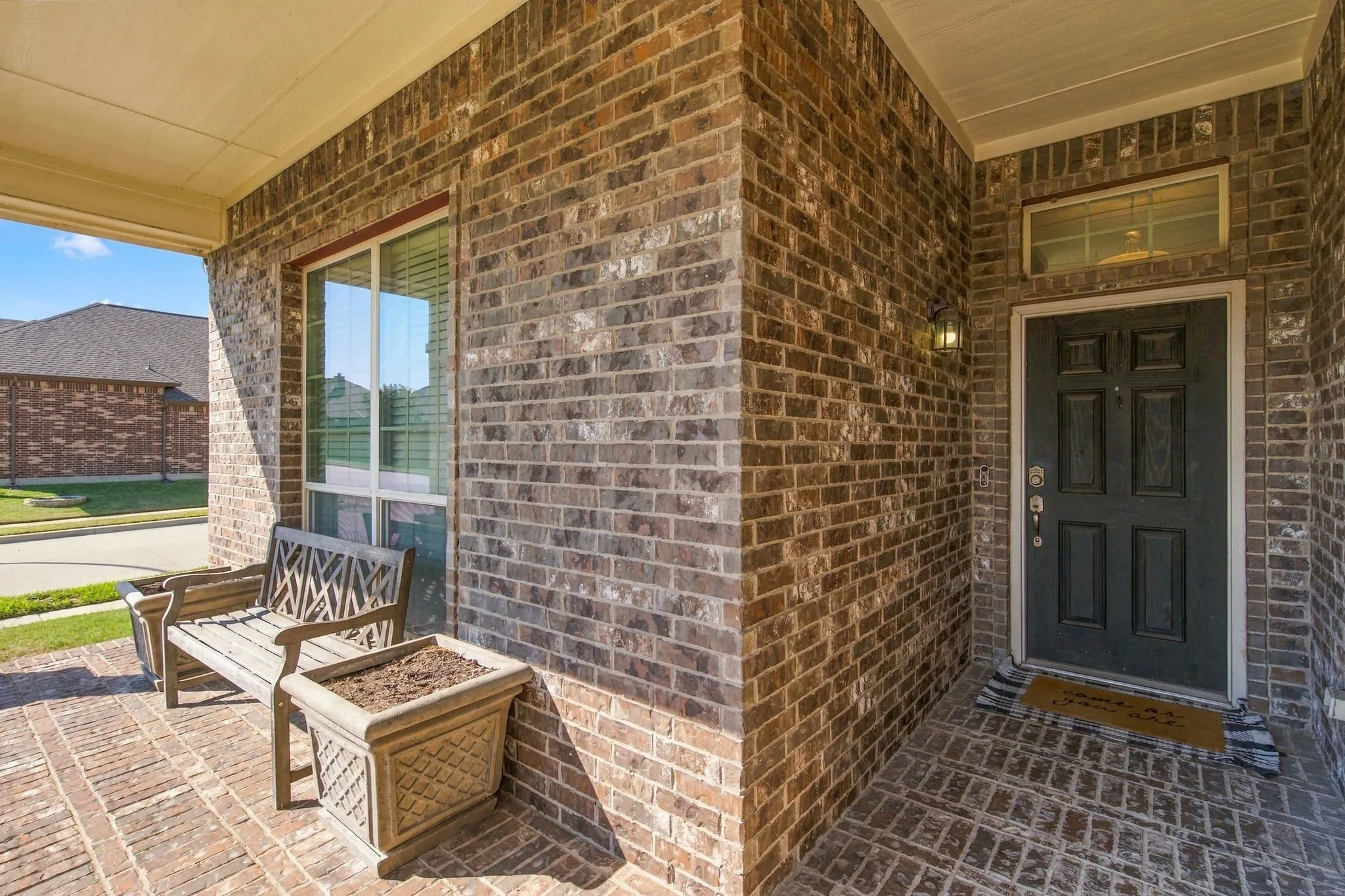 Brick exterior with a covered porch featuring a solid panel front door, a transom window, and a wall-mounted light fixture