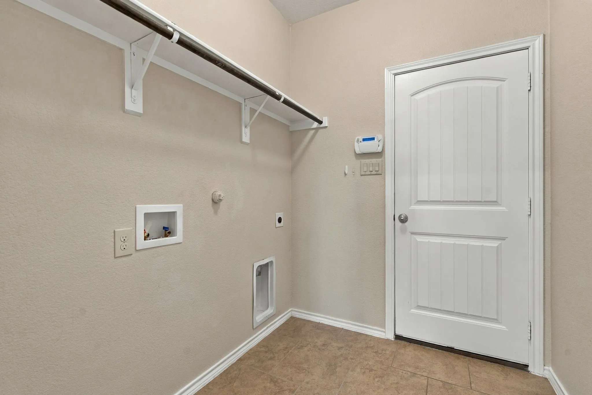 Laundry area featuring tile flooring, a built-in hanging rod with shelving, and utility hookups