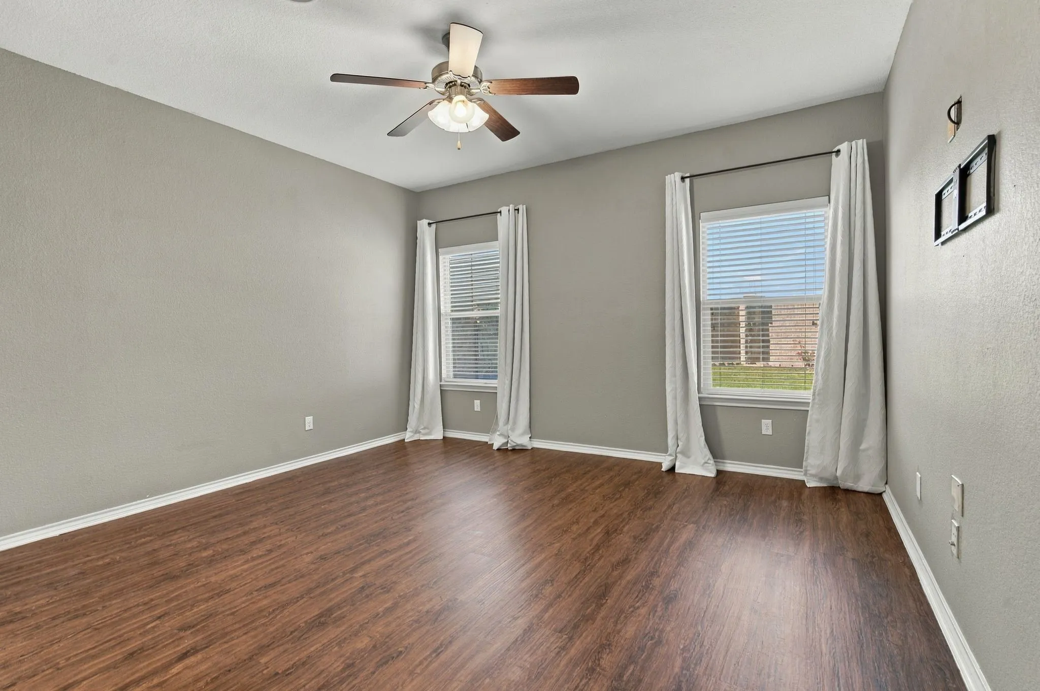Wood-finish flooring throughout, ceiling fan with integrated lighting, multiple windows with blinds, and neutral painted walls