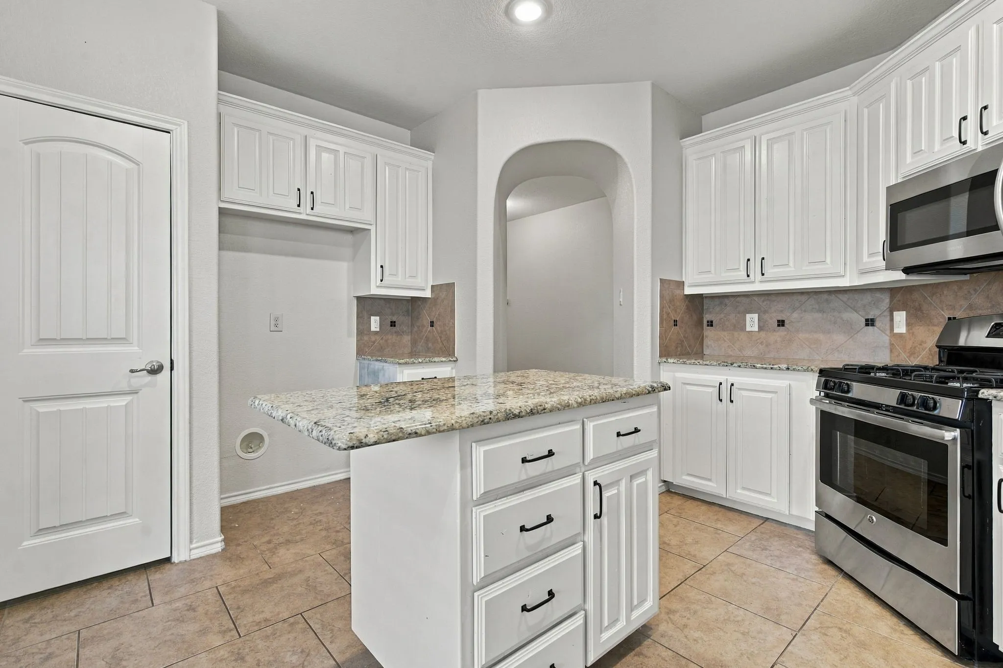 Kitchen featuring white cabinetry, a central island with a granite countertop, stainless steel appliances, and tile flooring